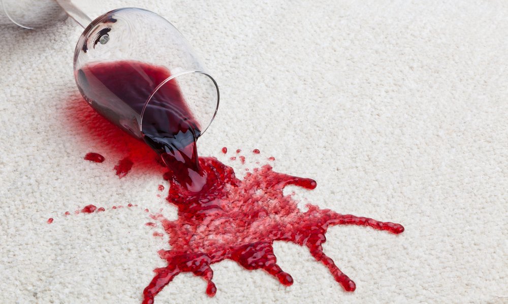 A glass of red wine spilling onto white carpeting